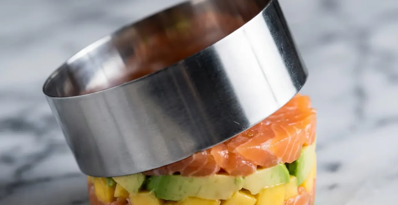 Mains de chef utilisant un cercle de montage pour dresser un tartare en couches colorées